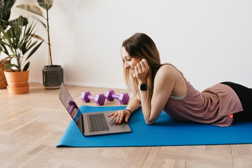 Woman lying on yoga mat looking at laptop while wearing a fitness tracker on wrist