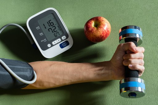 Photo of man's arm with blood pressure monitor cuff while holding a small weight next to an apple